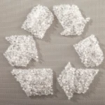 The picture shows small, clear plastic pellets arranged in the shape of the universal recycling symbol.